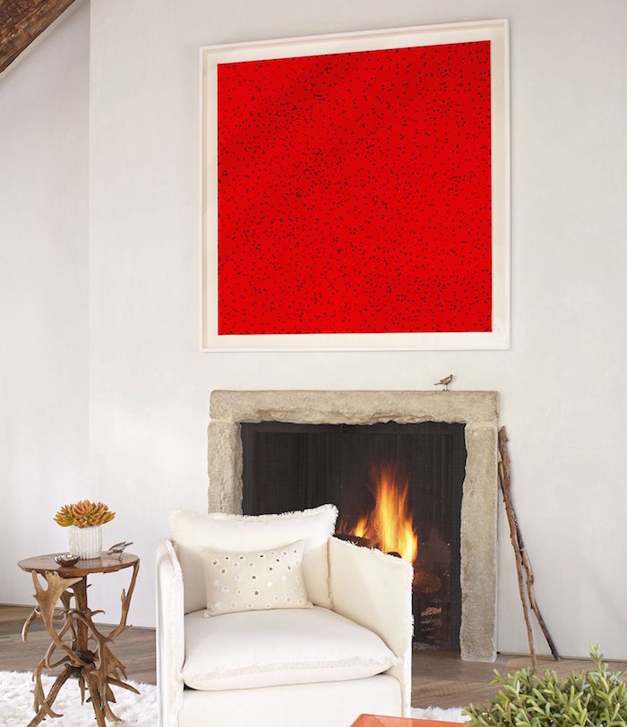 manteau de cheminée simple en pierre sur mur blanc et déco avec cadre abstrait rouge à pois et sol à parquet avec fauteuil blanc et table basse en bois design