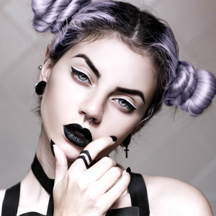 maquillage sorcière fille gothique aux cheveux couleur lilas assemblés en space buns, maquillage oeil de chat à l'eye liner blanc et noir