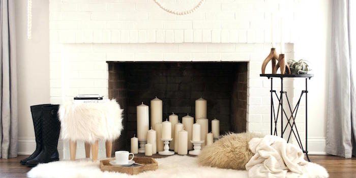 bougies dans foyer cheminée briques blanches avec tabouret à poils et coin cosy dans salon