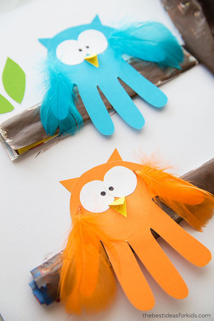 empreintes de main façon hibou aux ailes de plumes colorées, des yeux et bec en papier sur une bande de papier marron