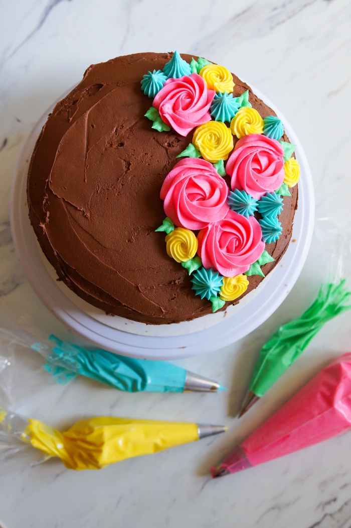 un simple gâteau recouvert de nappage au chocolat, décoré avec des fleurs au glacage sucre glace et beurre coloré réalisées à la poche à douille