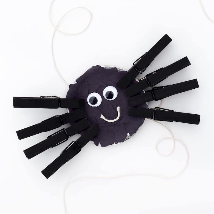 bricolage halloween maternelle, araignée en assiette de papier décorée de bouts de papier noir, pinces à linge repeints en noir et des yeux mobiles