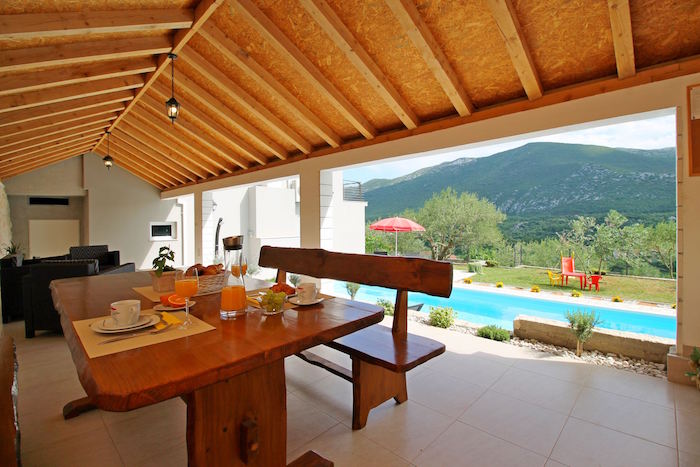 terrasse couverte en bois avec table et banc rustique dans maison avec piscine et vue sur montagne