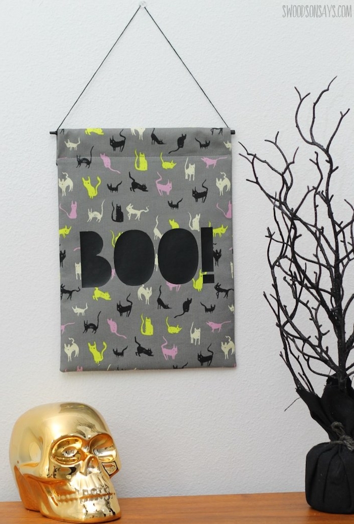 activités manuelles halloween, pan de tissu à motif chat décoré de lettres noires suspendu à un clou sur un mur, crâne couleur or