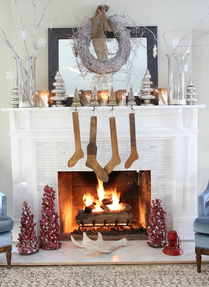 manteau de cheminée blanc à cadre en mosaique type crédence et déco sur thème hiver et noel avec objets décoratifs comme souliers en bois, min sapins rouges et bougeoirs design chrome et couronne grise