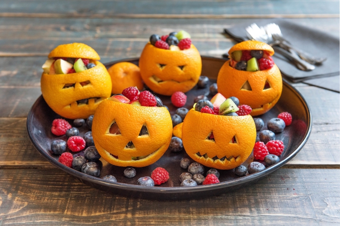 idée pour un dessert d'halloween santé, des bols citrouilles d'halloween réalisés avec des oranges, remplis de fruits rouges 