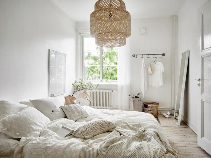 deco cocooning dans la chambre, plafonnier en rotin, grand lit blanc avec plusieurs coussins, sol de planches, miroir adossé