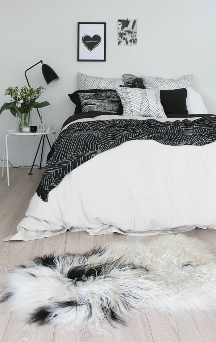 lit blanc et gris, table de chevet blanche, tapis fourrure, cadre peintures, sol en planches de bois, peinture murale couleur claire