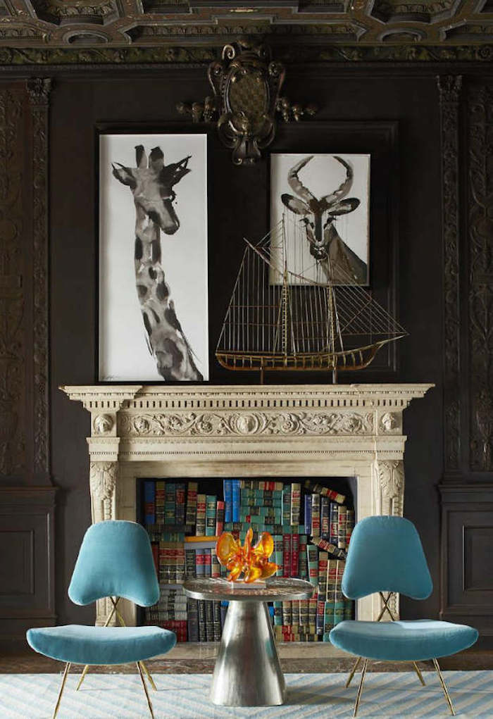 photo fausse cheminée décorative taillée comme support déco livres anciens maquette bateau, chaises retro en velours bleu