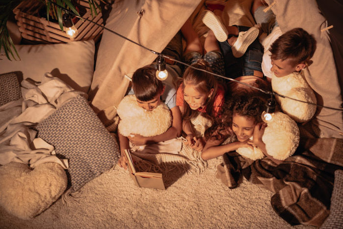 une soirée pyjama fête originale dans un tipi avec surplombé de guirlande lumineuse, enfants faisant une lecture collective