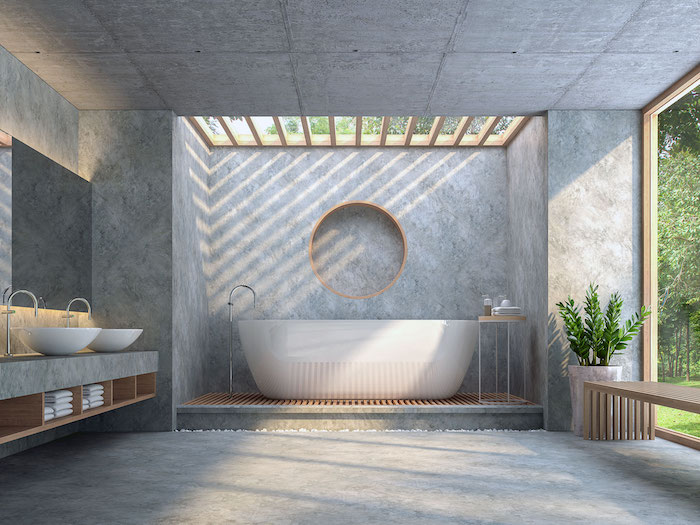 grande salle de bain ouverte avec baie vitrée sur jardin, sol murs et plafond en béton avec baignoire ilot