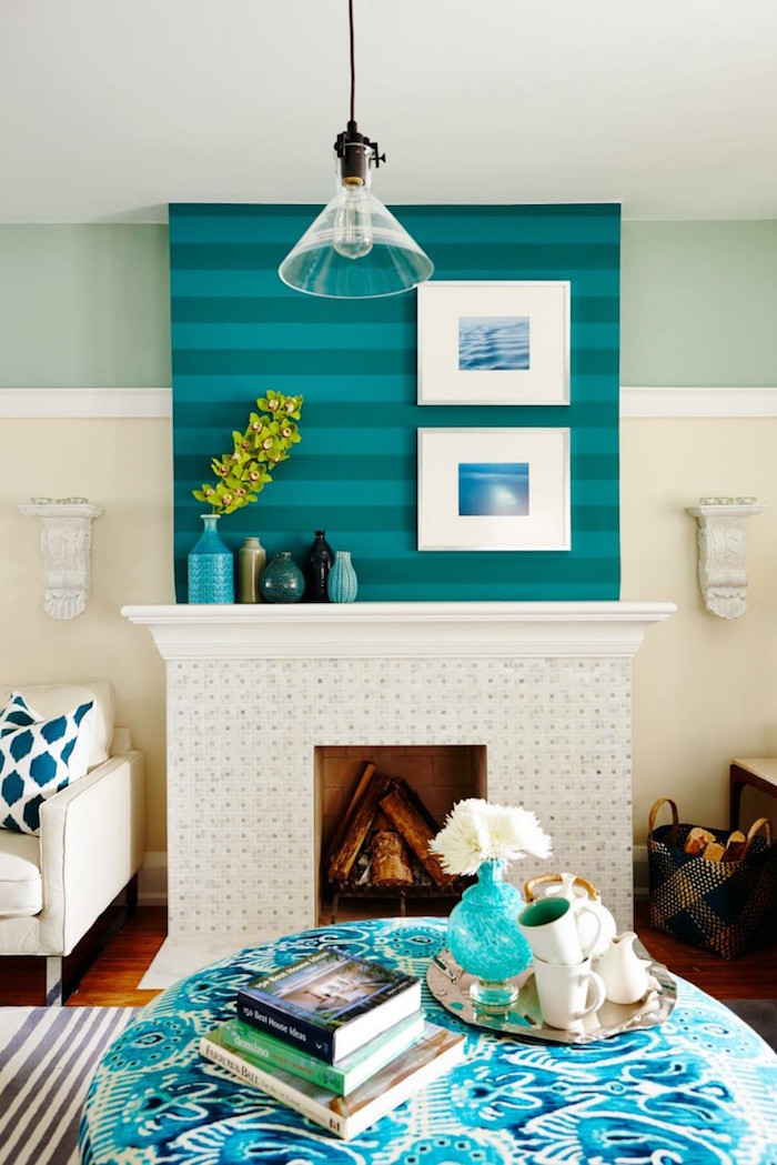 décoration de cheminée avec manteau blanc large sous mur bleu à rayures et cadres blancs avec photos d'ocean, table de salon ronde bleu et blanc