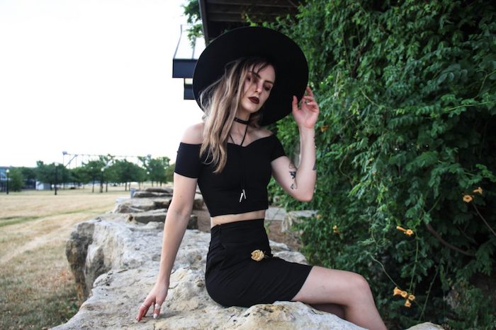 déguisement sorcière femme moderne avec un crop top noir, jupe noire et capeline à larges bords, collier ras du cou, maquillage foncé