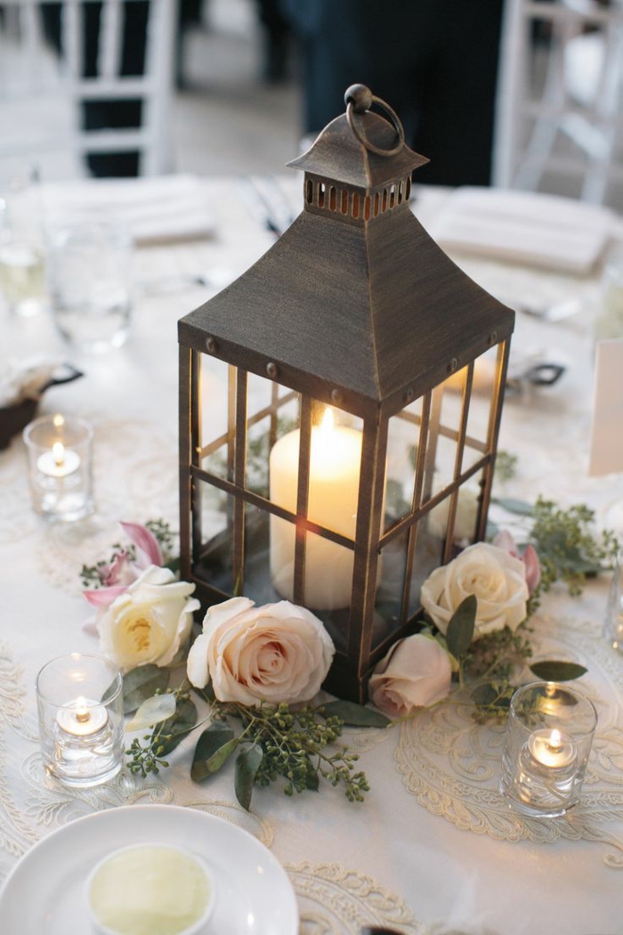 table de mariage joliment décorée, lanterne métallique, bougie blanche, roses et bougies flottantes