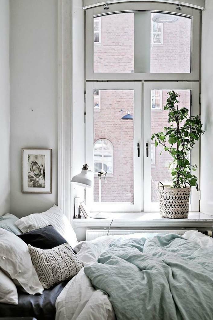 lit cosy dans une chambre blanche et lumineuse, cache-pot rustique, cadre peinture gris et blanc, plante verte, lampe de table blanche