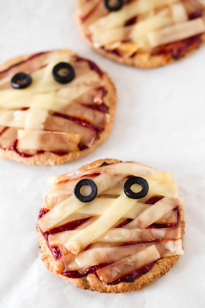 des minis pizzas apéritives à la tomate et au fromage vegan en forme de petites momies d'halloween, bouchées apéritives pour un repas halloween aussi savoureux qu'effrayant