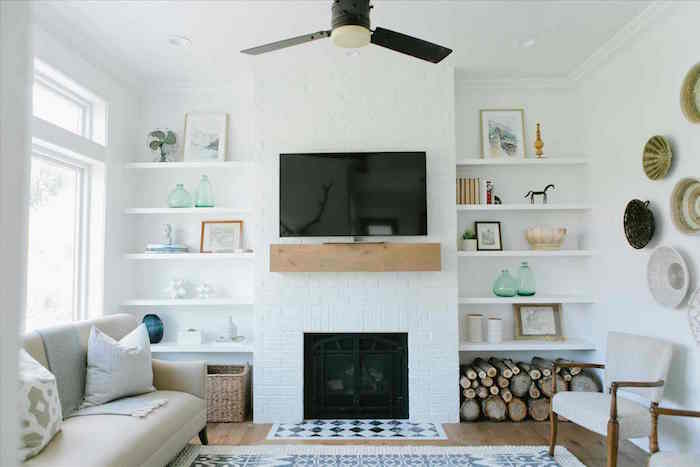 cheminée fermée moderne incrustée avec cadre blanc et étagère poutre bois comme support tv, murs blancs avec étagères et plats suspendus