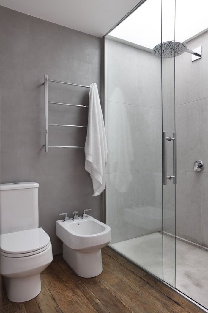 salle de bain avec murs en béton ciré ciment, douche italienne et sol en parquet avec toilettes et bidet