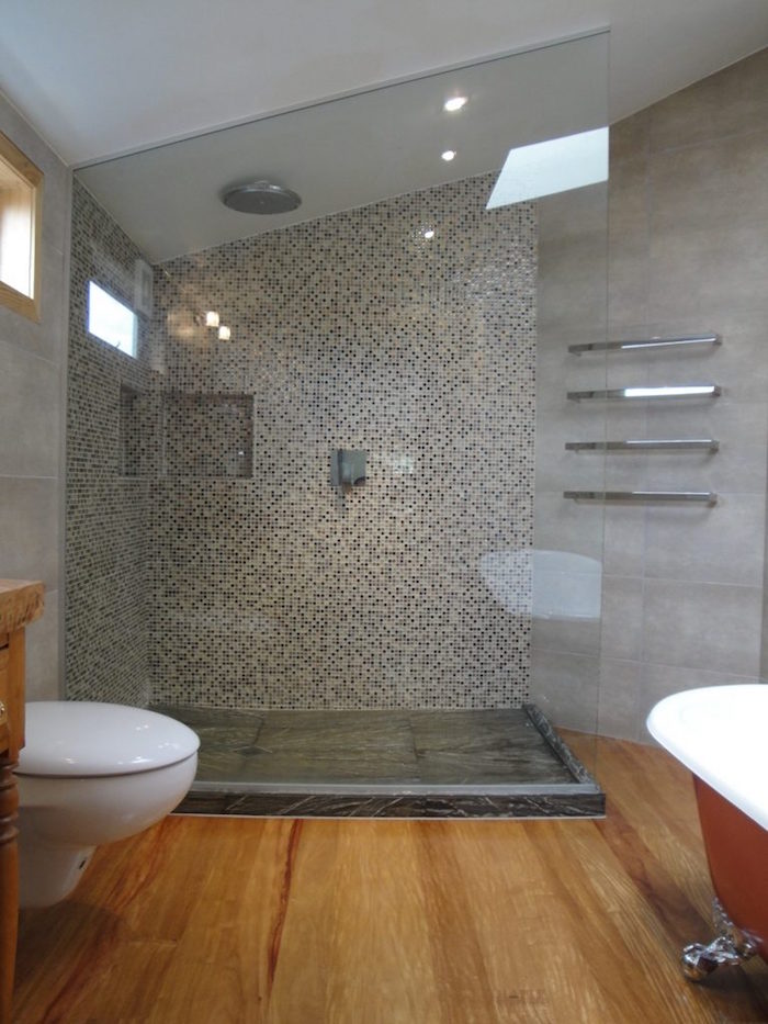 salle de bain moderne mansardée avec mur en ciment gris, douche italienne et sol en bois avec baignoire ilot