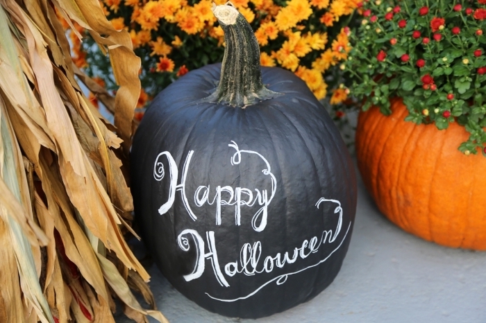 exemple de décoration extérieure pour la fête d'Halloween avec citrouille peinte en noire à lettres blanches