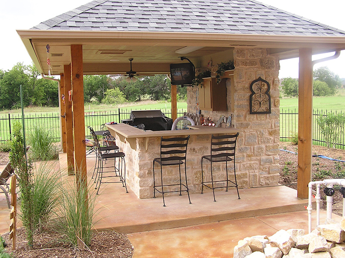 petit espace cuisine d'été extérieure couverte en pierres, dans jardin avec toiture pergola en bois