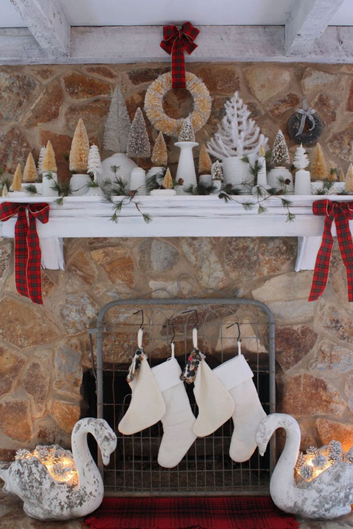 deco de noel sur cheminée en pierres avec étagère blanche en bois et objets decoratifs chaussettes, bougies et mini sapins