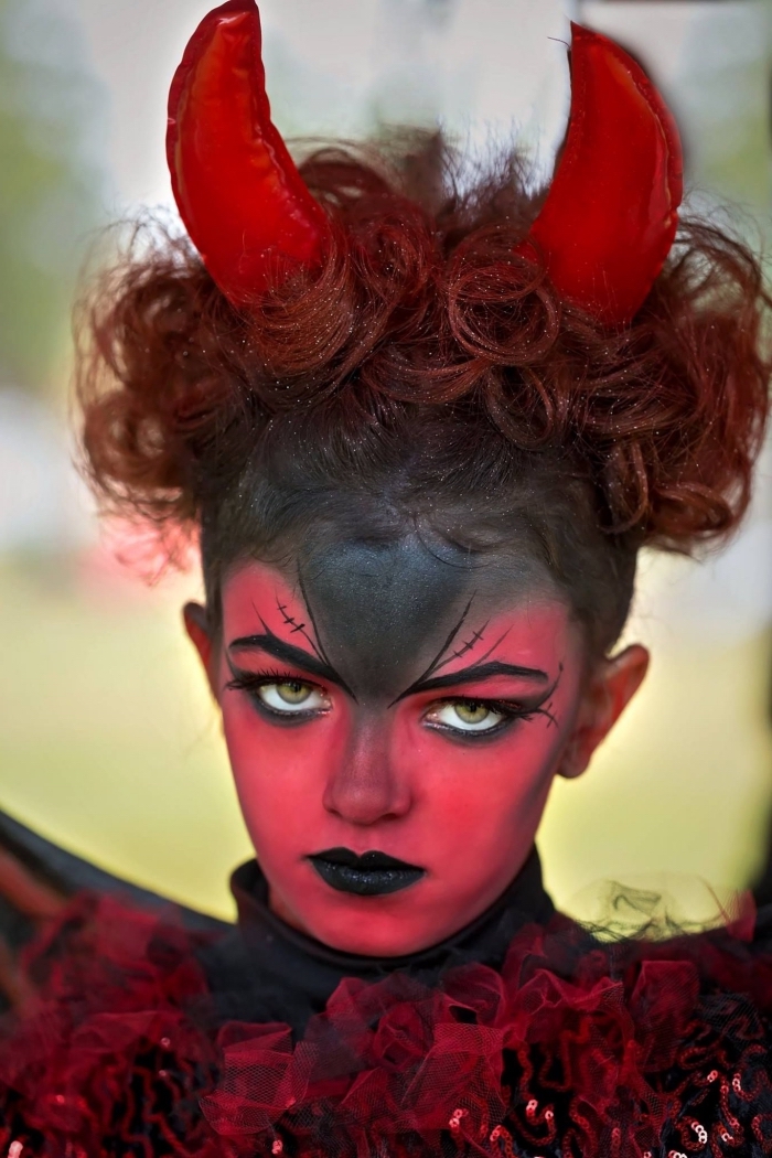idée pour un deguisement halloween fille original, maquillage petite diablesse à peau peinte en rouge et noir avec des yeux sourcils en cornes du diable, bouche noire et des yeux soulignés de noir