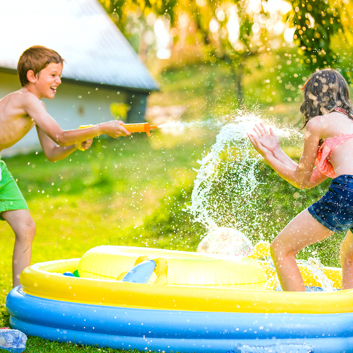 anniversaire 10 ans en plein air pendant l été, jeu avec des pistolet à eau autour d une piscine gonflable sur un gazon vert