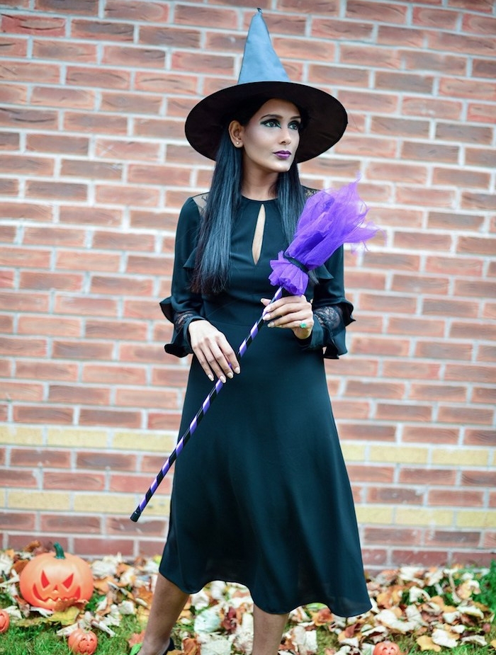 tenue sorcière en robe noire longue avec manches, chapeau de sorciere classique, balai magique en tulle, maqulillage foncé dramatique avec des ombres yeux foncés