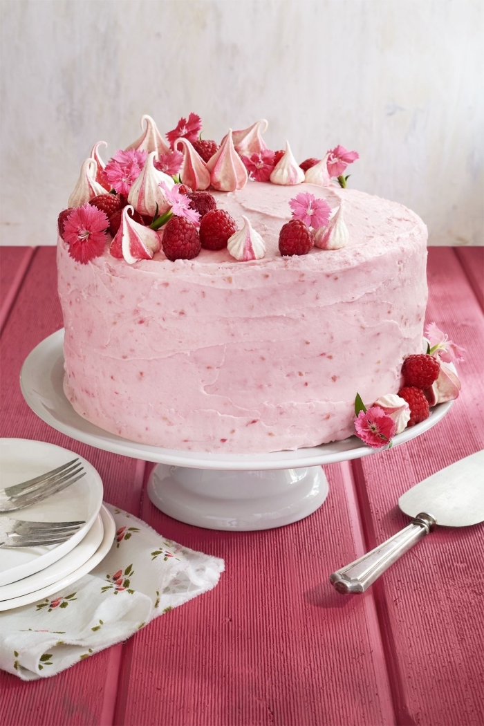 joli gâteau d'anniversaire au glacage framboise et crème au beurre, décoré avec des meringues colorées rose et des framboises fraîches