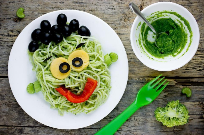 recette d'halloween facile pour régaler les enfants, des pâtes frankenstein au pesto vert, décorées avec des légumes et des olives