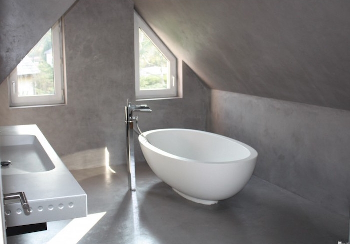 salle de bain mansardée dans combles recouverte de béton avec baignoire ilot ovale