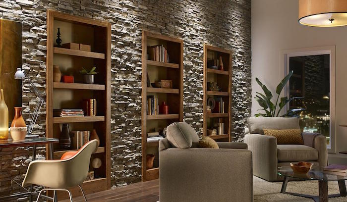 mur de salon couvert de plaquettes de pierres de parement grises entourant étagères et bibliothèques en bois