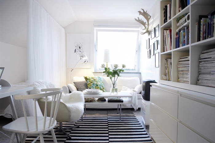 ambiance cosy dans un petit salon blanc dynamisé par un tapis à rayures, coin de lecture avec un fauteuil cosy accessoirisé d'une fausse fourrure blanche