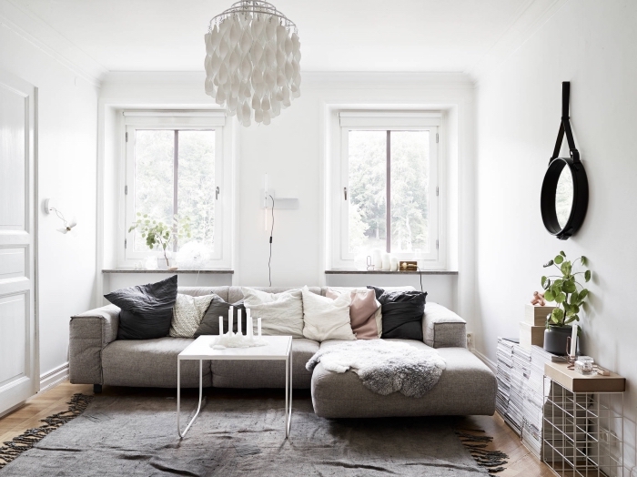 petit salon scandinave monochrome avec un canapé cosy gris recouvert de coussins décoratifs en lin et un tapis frangé