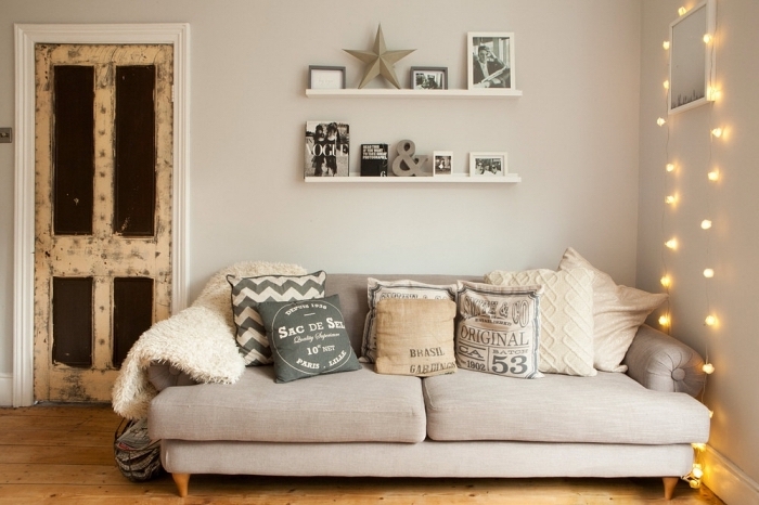petit coin de détente avec un canapé cosy beige recouvert de coussins décoratifs cocooning de la même tonalité et une déco de guirlande lumineuse suspendue au mur