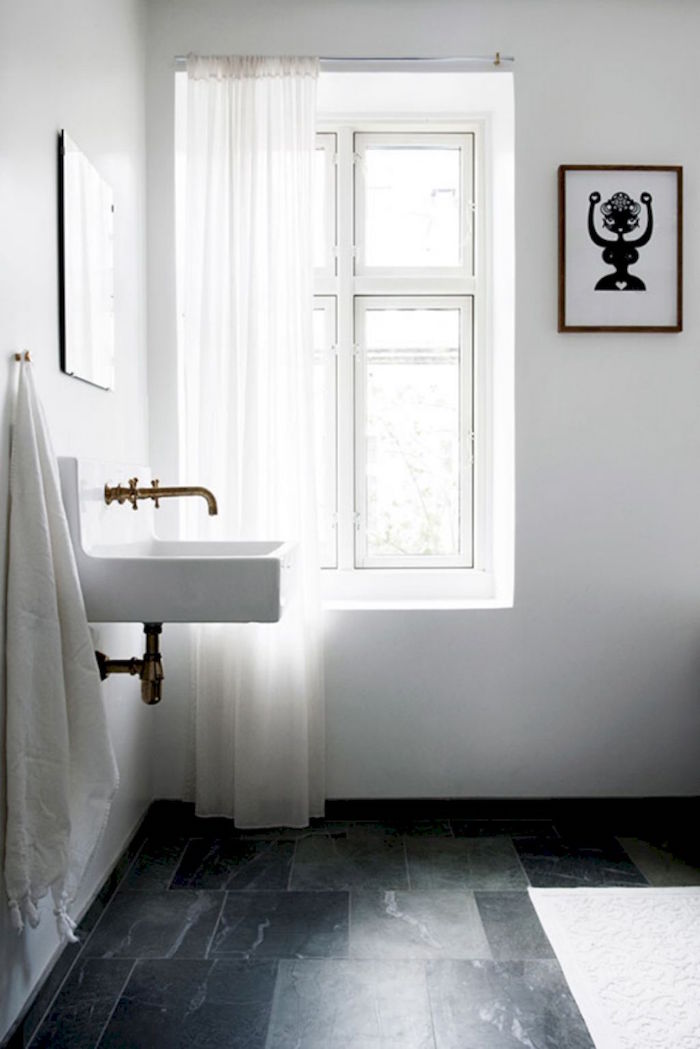 salle de bain minimaliste suedoise avec lavabo carré vintage et plomberie cuivre or retro sur sol carrelage foncé marbré et murs blancs