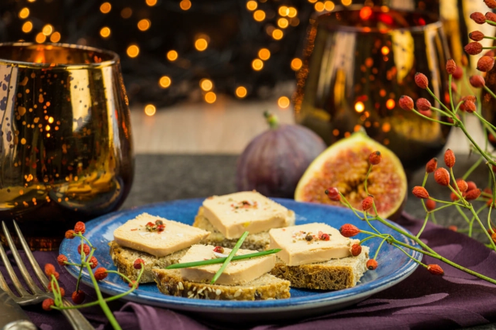 tranches de pain au fromage et aux figues, verres à vin, assiette bleue, fourchette, décoration avec brins d'églantier 