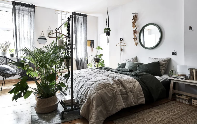 bout de lit en plante exotique d intérieur monstera palmier dans un panier rotin linge de lit gris et noir miroir rond sur mur blanc chaise noire metallique