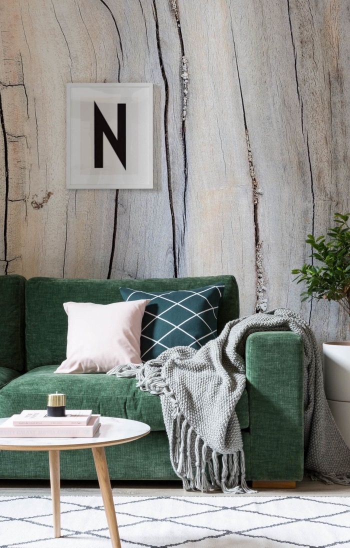 canapé cosy vert accessoirisé avec des coussins unis ou graphiques en vert et rose, posé contre un mur recouvert de papier peint trompe-l'oeil effet bois