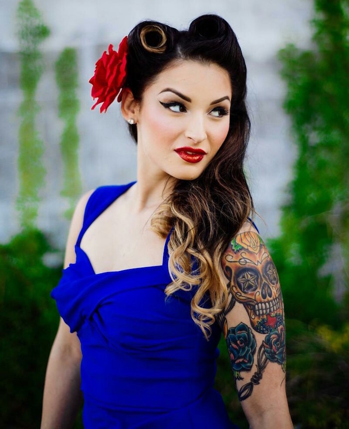 femme en robe bleu roi avec tatouage calavera sur l'épaule, coiffure pin up en rouleau victory rolls et maquillage année 50