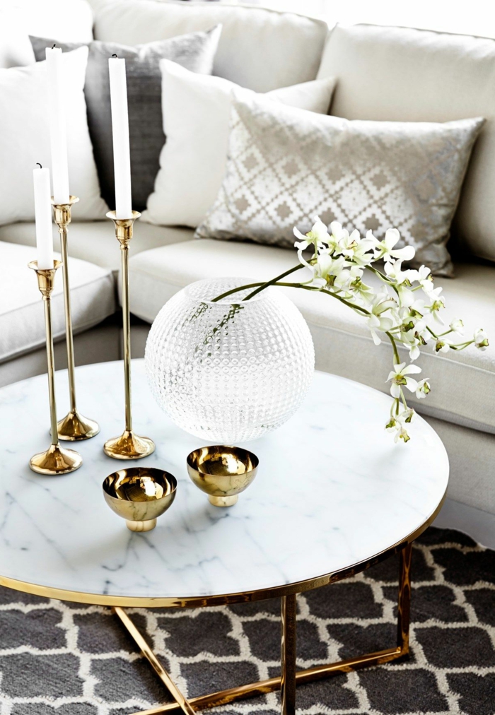 deco table basse marbre, jolis bougeoirs dorés, bougies blanches, vase boule en verre, coussins gris, deux brins de fleurs