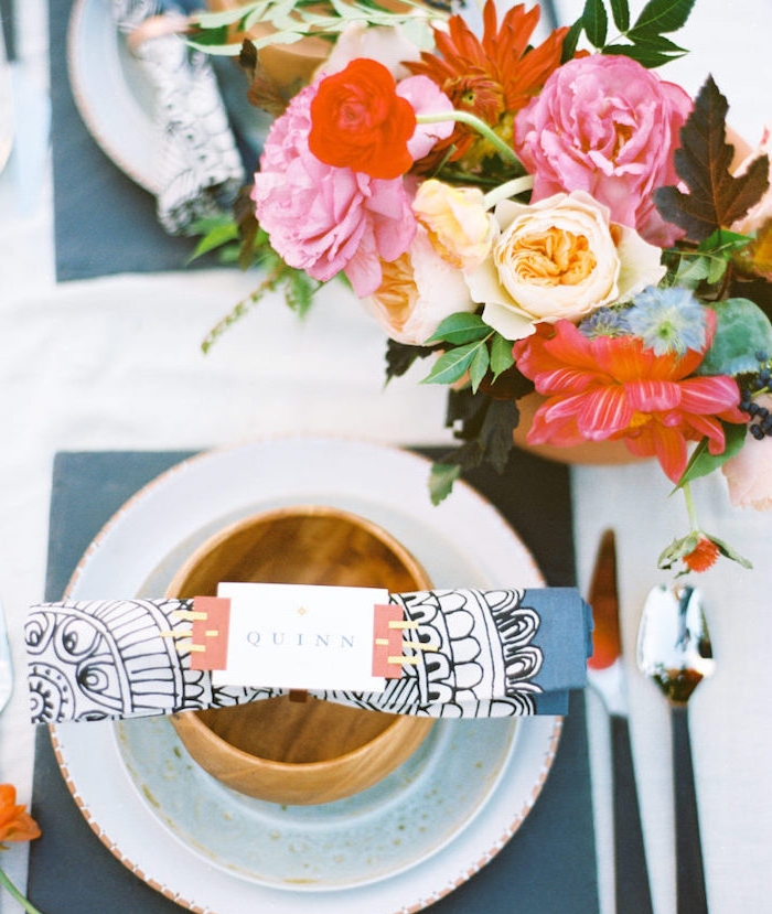 exemple de pliage de serviette en papier à motifs mandala dans assiette sur serviette carré gris, centre de table en bouquet de fleurs colorées