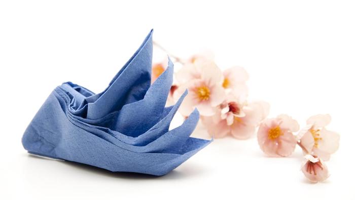 pliage de serviette en papier en forme de cygne bleu marine avec une decoration florale de brin d orchidée
