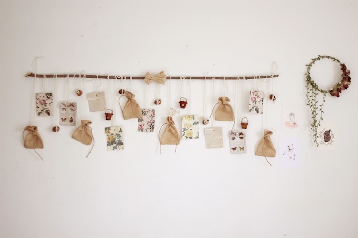 branche de bois flotté sur mur blanc avec petits sachets cadeau et différentes décorations vintage chic, couronne de noel fleurs séchées, calendrier de l avent a faire soi meme