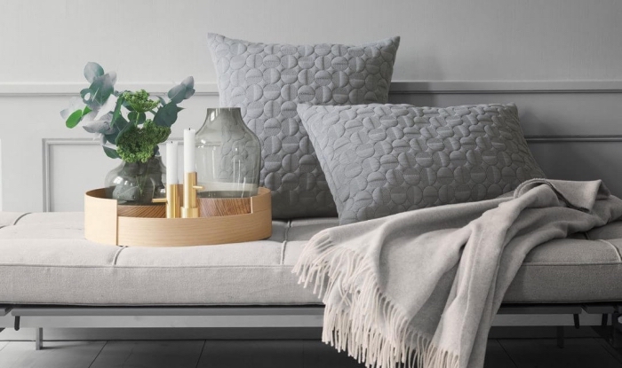 les accessoires indispensables pour un salon hygge deco scandinave, coussins gris à motifs texturés, une couverture douillette et un joli plateau déco en bois avec un petit vase en céramique