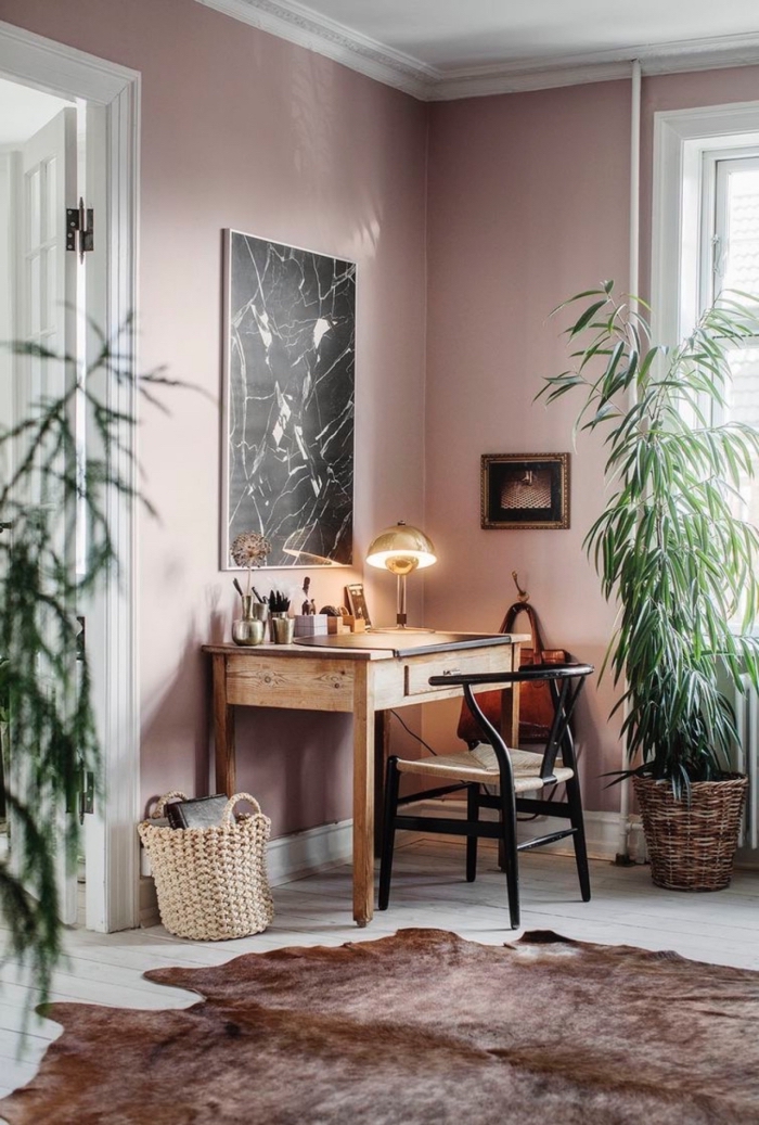 un coin bureau en bois et noir aménagé dans un salon rose poudré cocooning au sol boisé blanc, tapis de peau de bête pour un accent authentique dans le salon