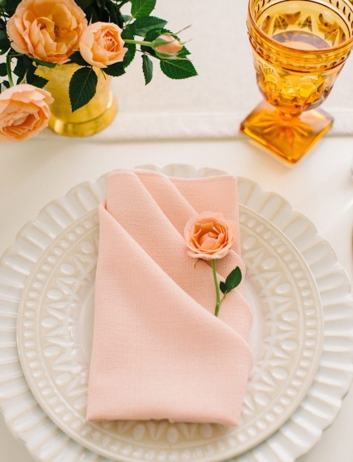 modele de pliage de serviette facile en tissu rose, pliage range couvert avec decoration petite rose dans assiettes blanches, centre de table en bouquet de roses