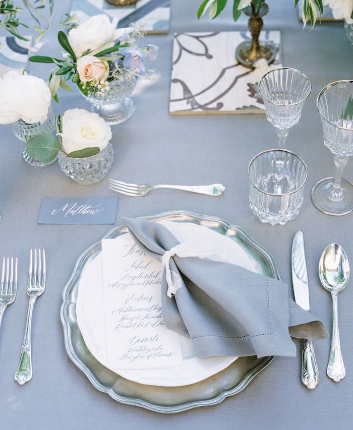 table revêtue de nappe grise avec de petits bouquets de fleurs, couverts argent et vaisselle vintage, deco mariage champetre