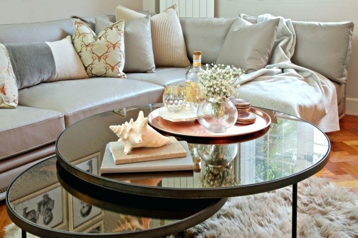 tables gigognes rondes, tapis poilu, coussins neutres, plateau cuivré avec vases, livres et coquillage, sofa d'angle gris